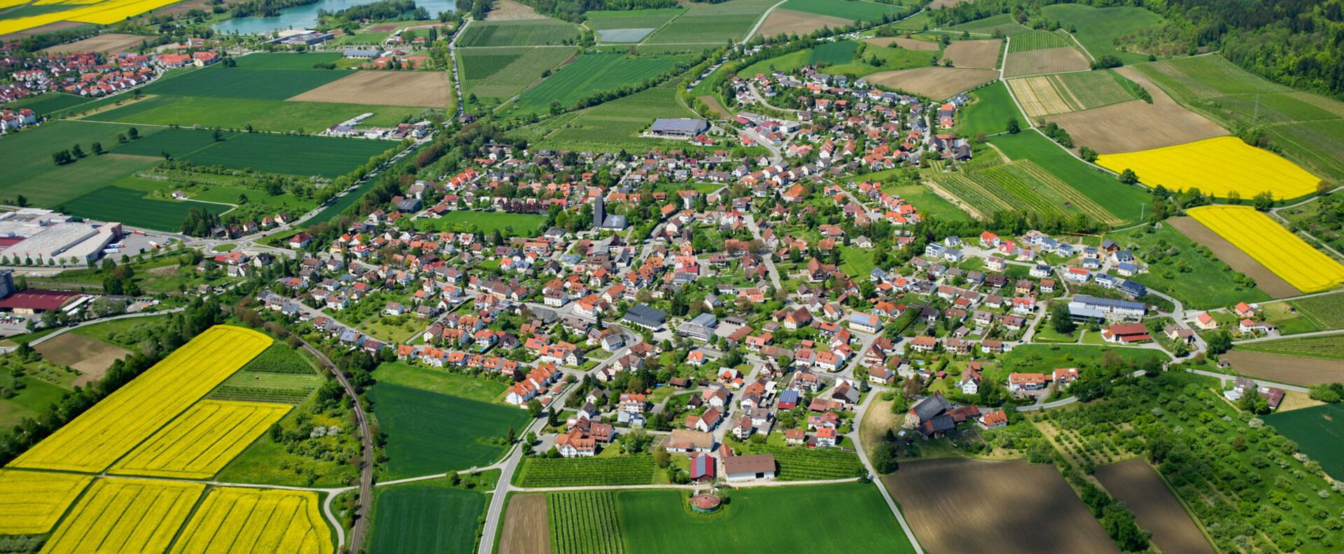 Häuser zum Kauf & Verkauf in der Nähe des Bodensee Luftbild einer Stadt umgeben von grünen Agrarflächen & gelben Rapsfeldern - Region Bodensee